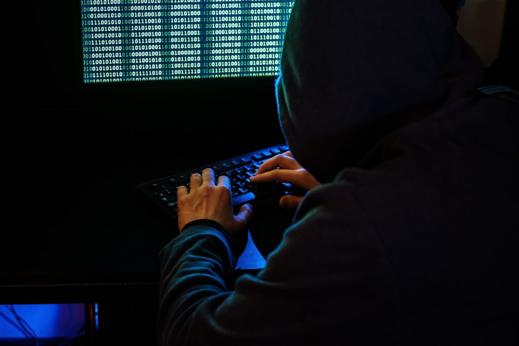 Hacker encapuzado mexendo em um computador.